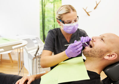 Zahnarzthelferin schaut in den Mund eines Patienten
